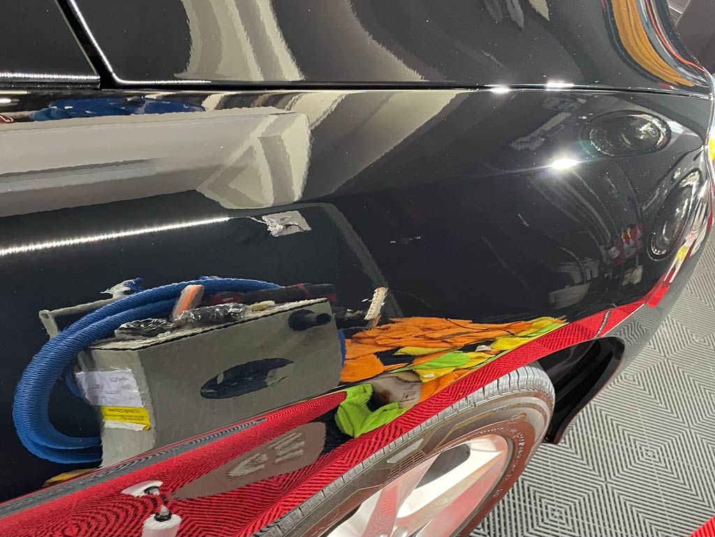 Close-up of a shiny black car's side, reflecting objects in a garage.