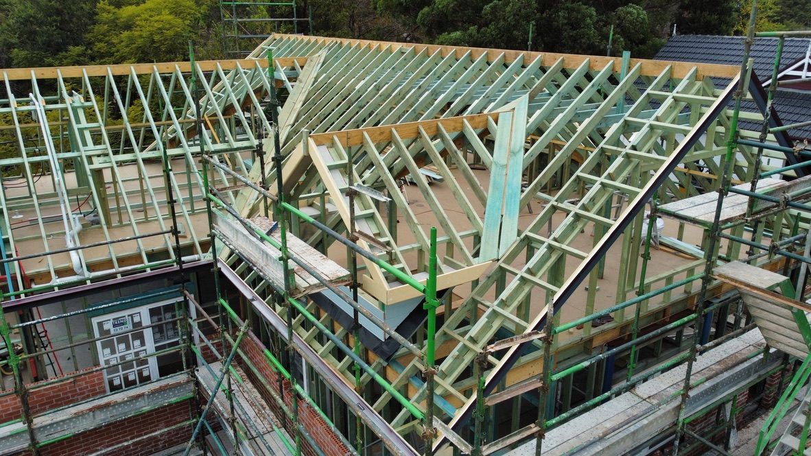 Partially constructed house with exposed wooden roof trusses and scaffolding around the exterior