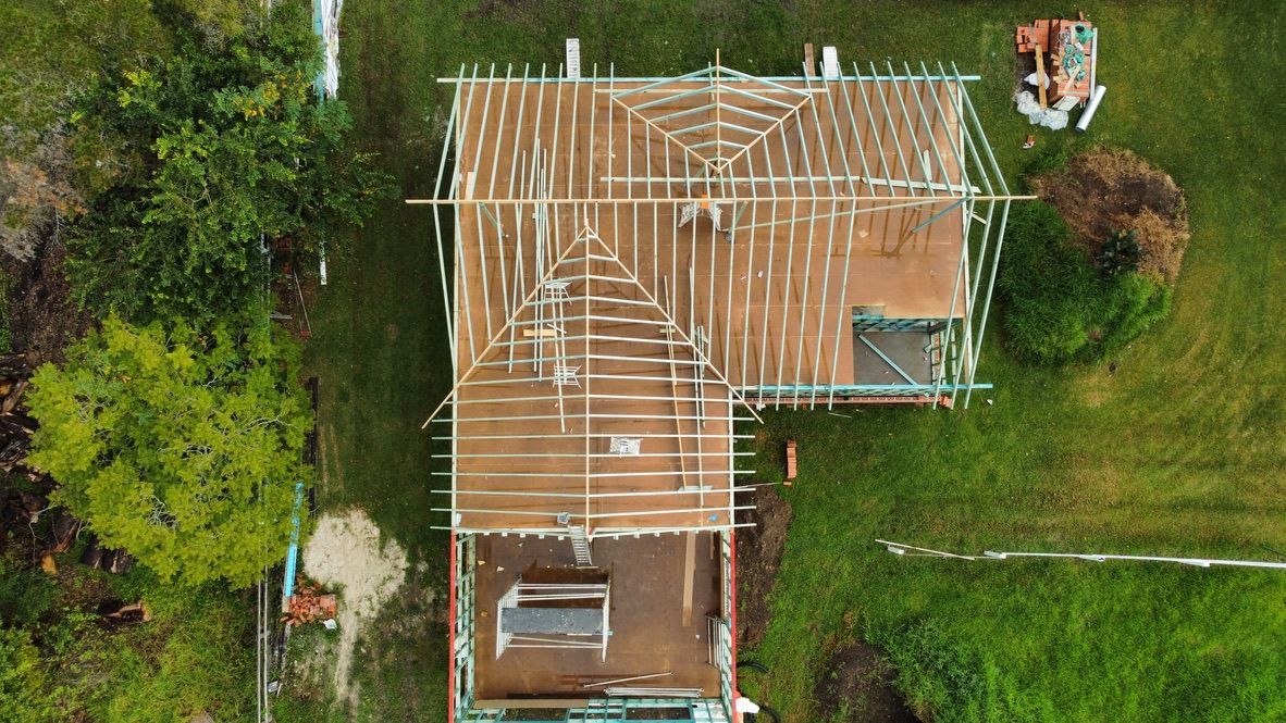 Partially built house with wooden roof framing and green scaffolding around the structure