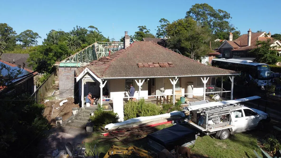 Aerial view of a house under construction beside red-roofed homes and trees.
