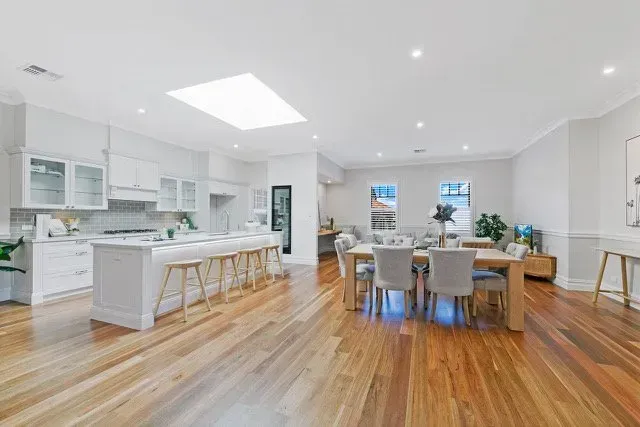 Bright open-plan kitchen and dining room with wood floors, white cabinets, and a long table with chairs.