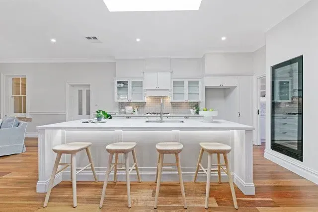Bright white kitchen with island, four stools, and hardwood floors