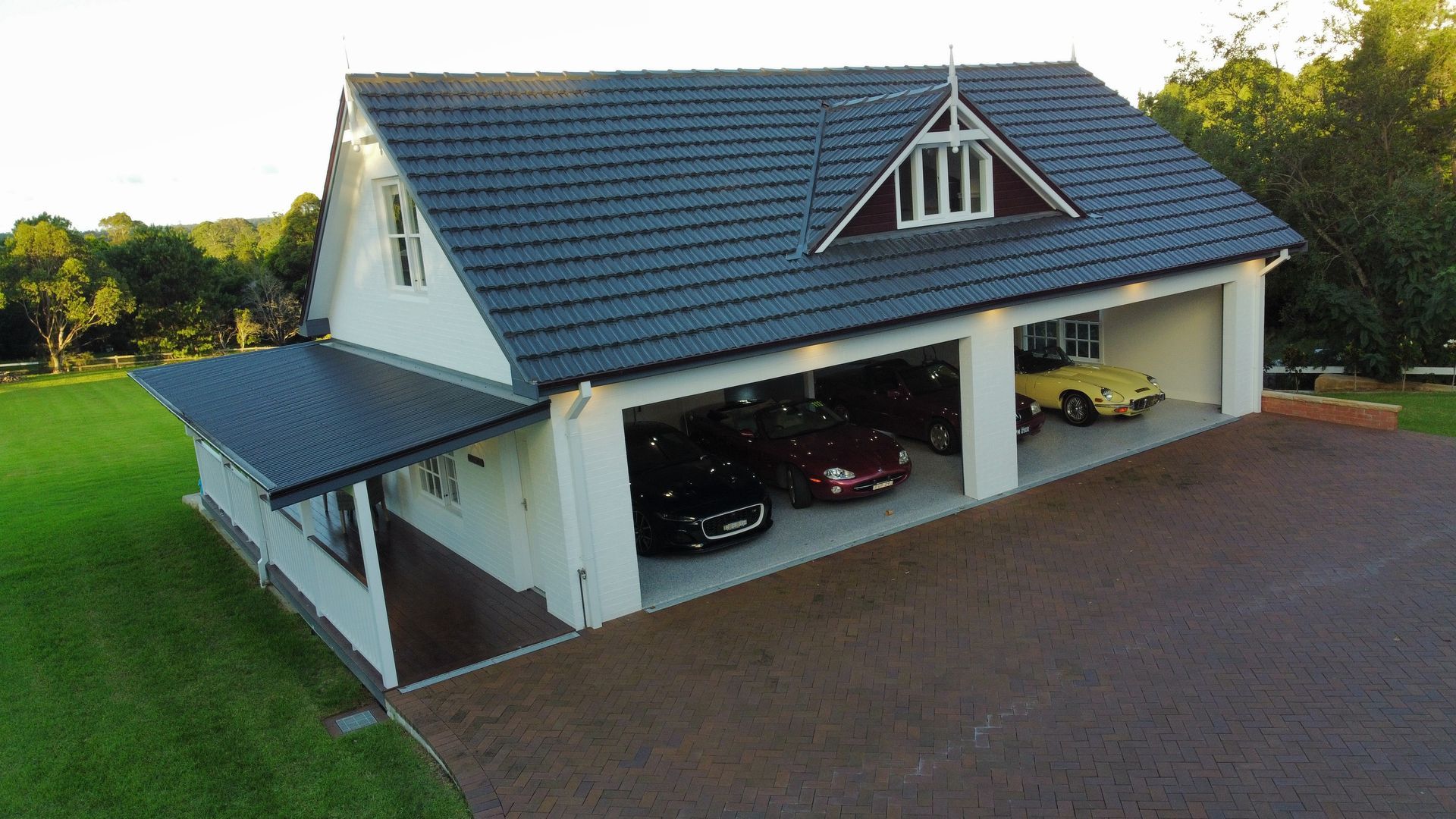 Modern house with large open garage, dark roof, white walls, and green lawn at dusk