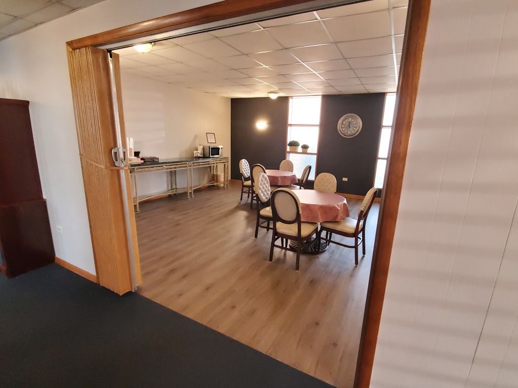 A doorway into a dining area with tables, chairs, and a serving counter with a microwave and food.