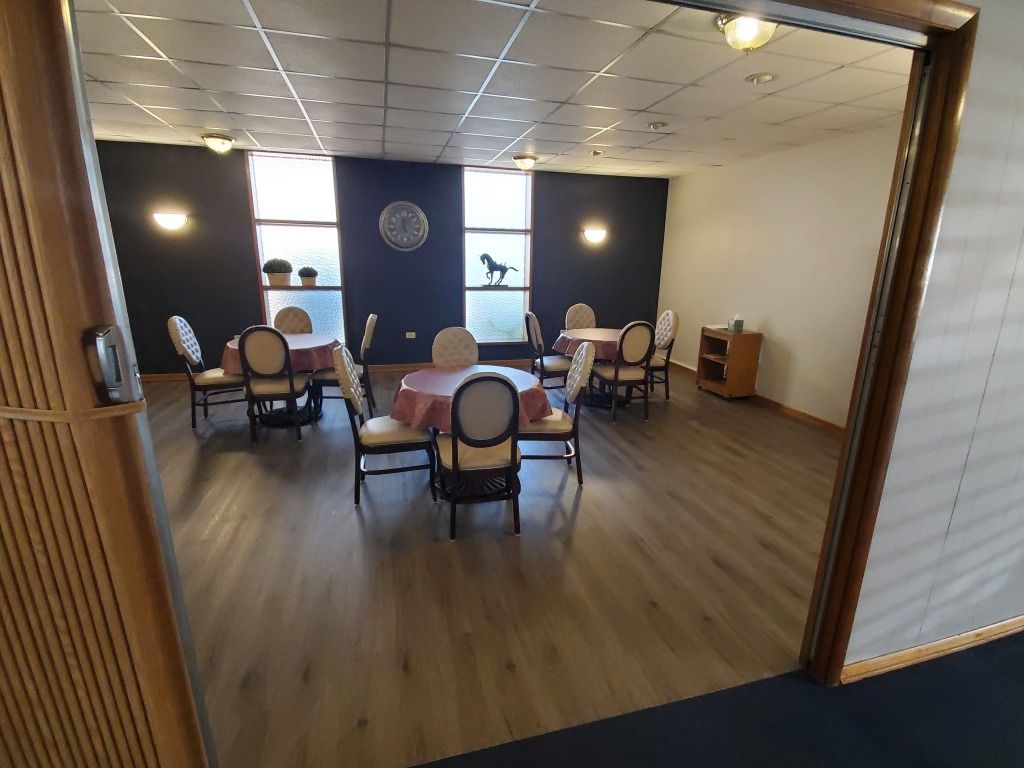 Dining room with round tables, chairs, and dark blue accent walls. Window with horse silhouette. Wooden floor.