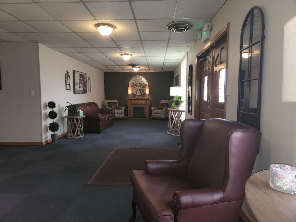 Lobby with burgundy armchairs, sofas, dark carpet, and a fireplace. Doors, mirrors, and lamps are also visible.