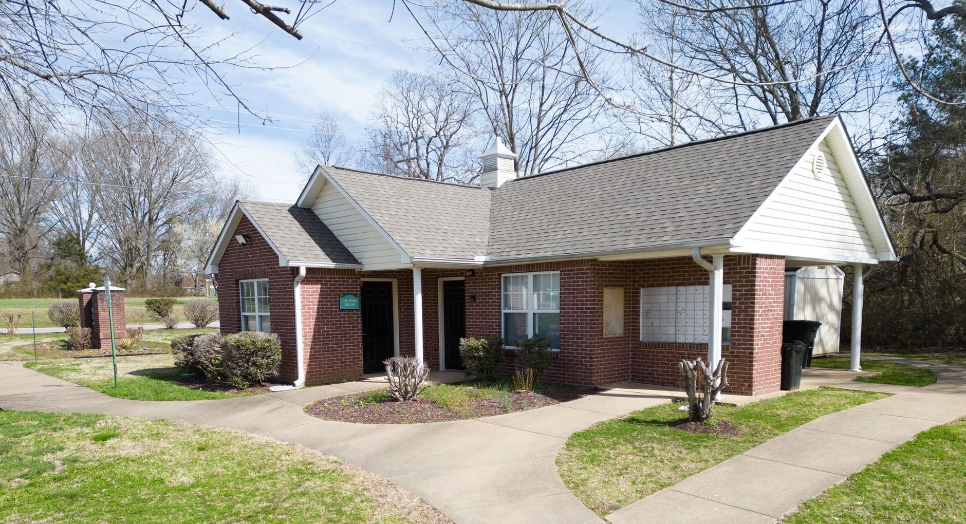 A small brick house with a gray roof and a walkway leading to it.