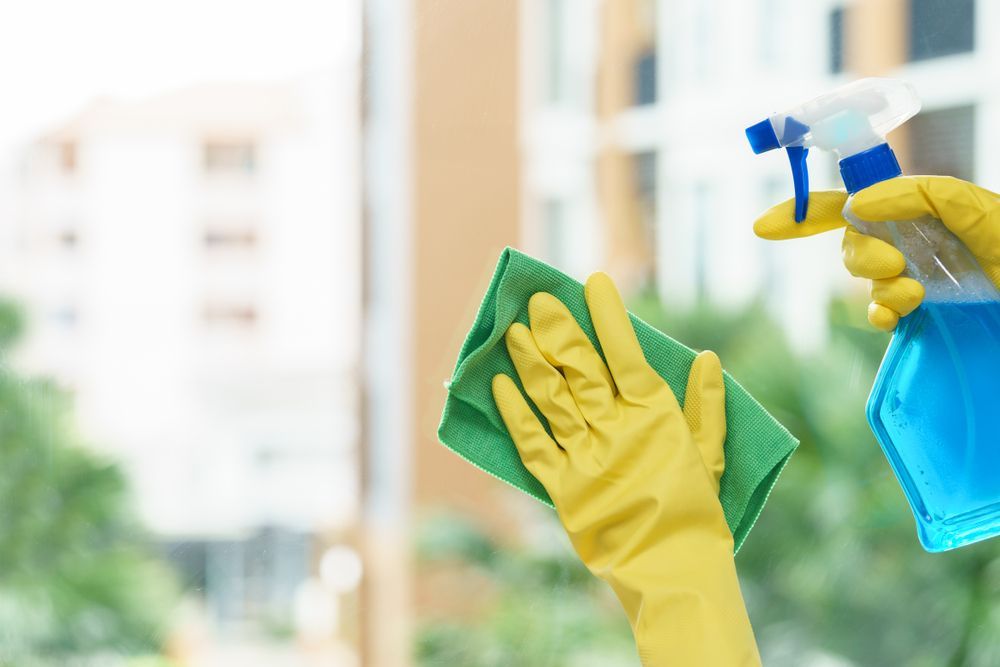 Hands in Yellow Gloves Cleaning a Window With Spray Bottle and Green Cloth — Integral Cleaning Services in Aberdare, NSW