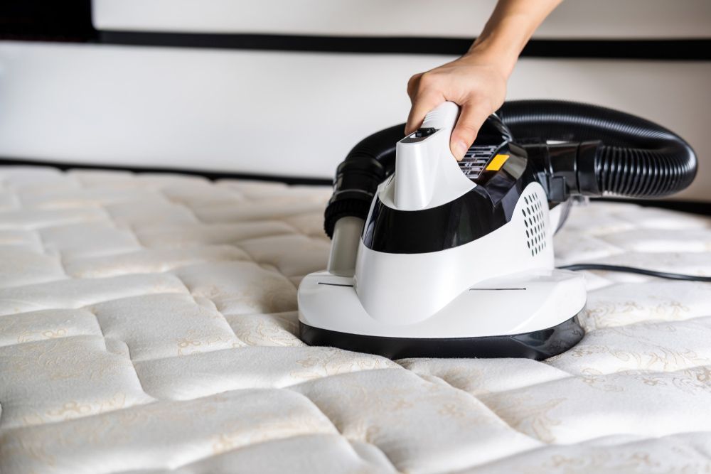 Person Vacuuming a White Quilted Mattress With a Handheld Device — Integral Cleaning Services in Hunter Valley, NSW