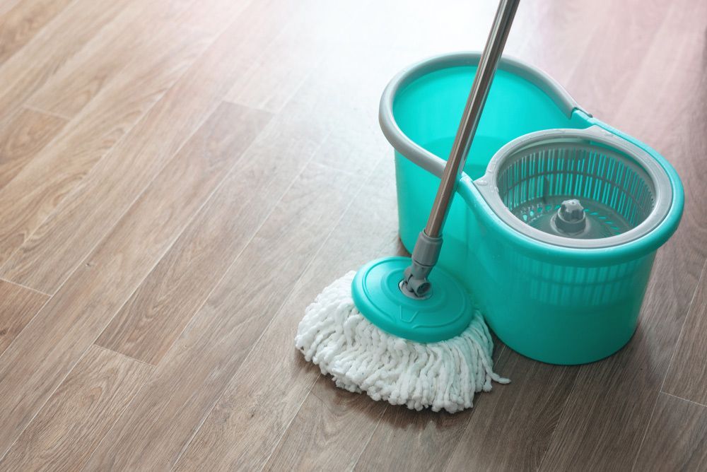 A Turquoise Mop and Bucket Set on a Light Brown Wooden Floor — Integral Cleaning Services in Aberdare, NSW