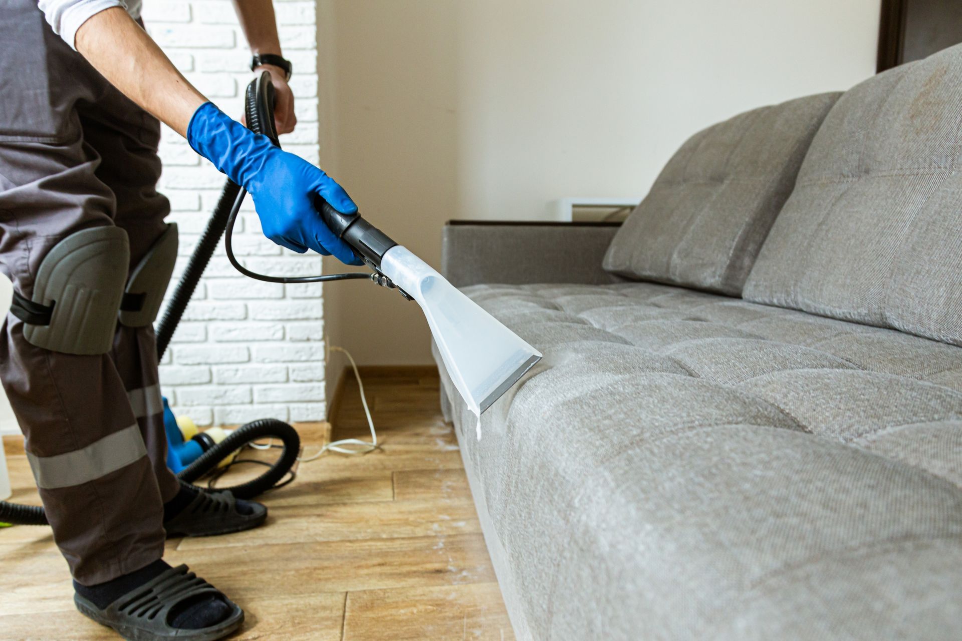 Person Cleaning a Grey Couch With a Steam Cleaner in a Room — Integral Cleaning Services in Maitland, NSW