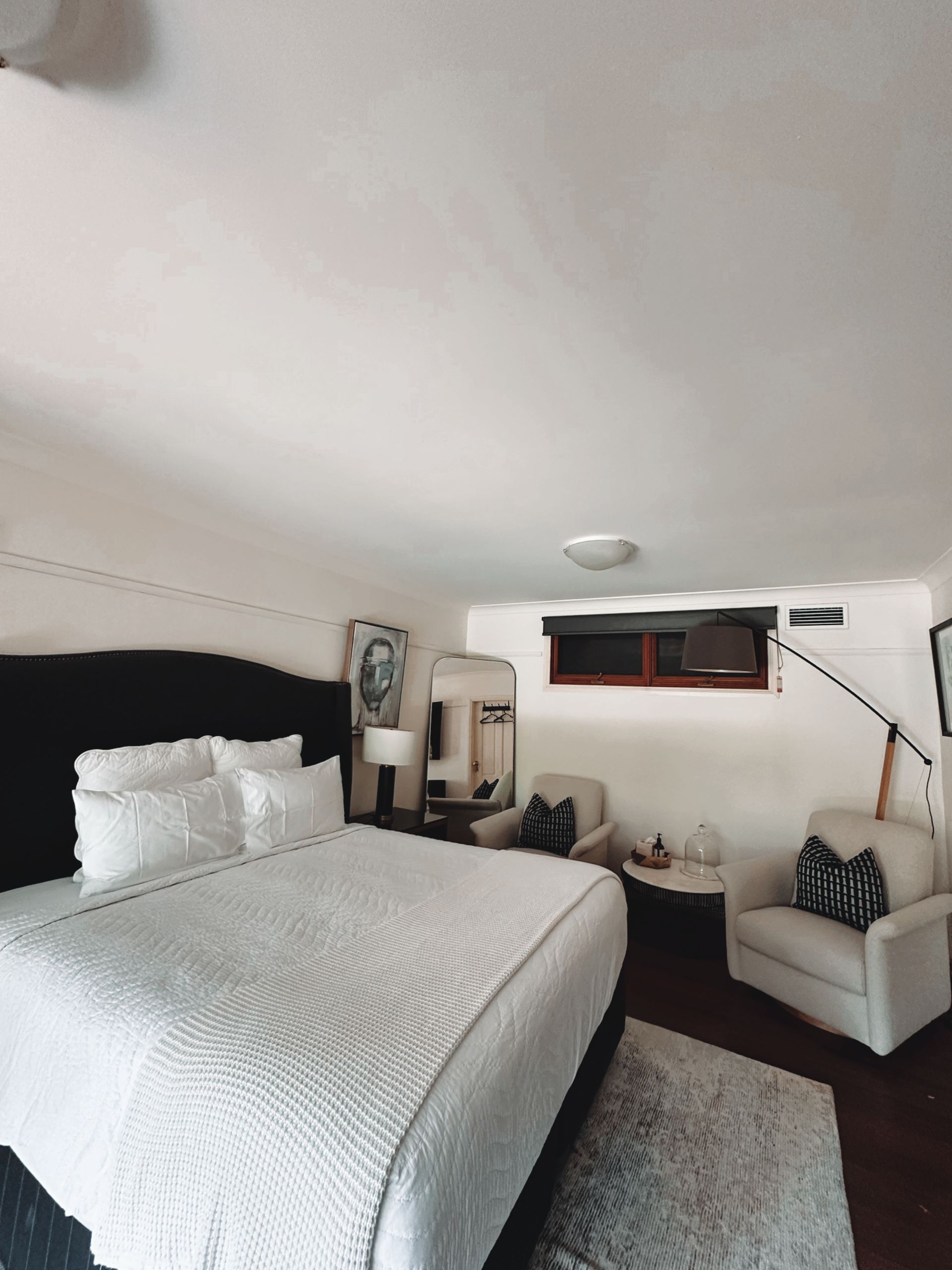 Bedroom with a large bed, two armchairs, a rug, and a mirror. White and black decor, small window  — Integral Cleaning Services in Aberdare, NSW