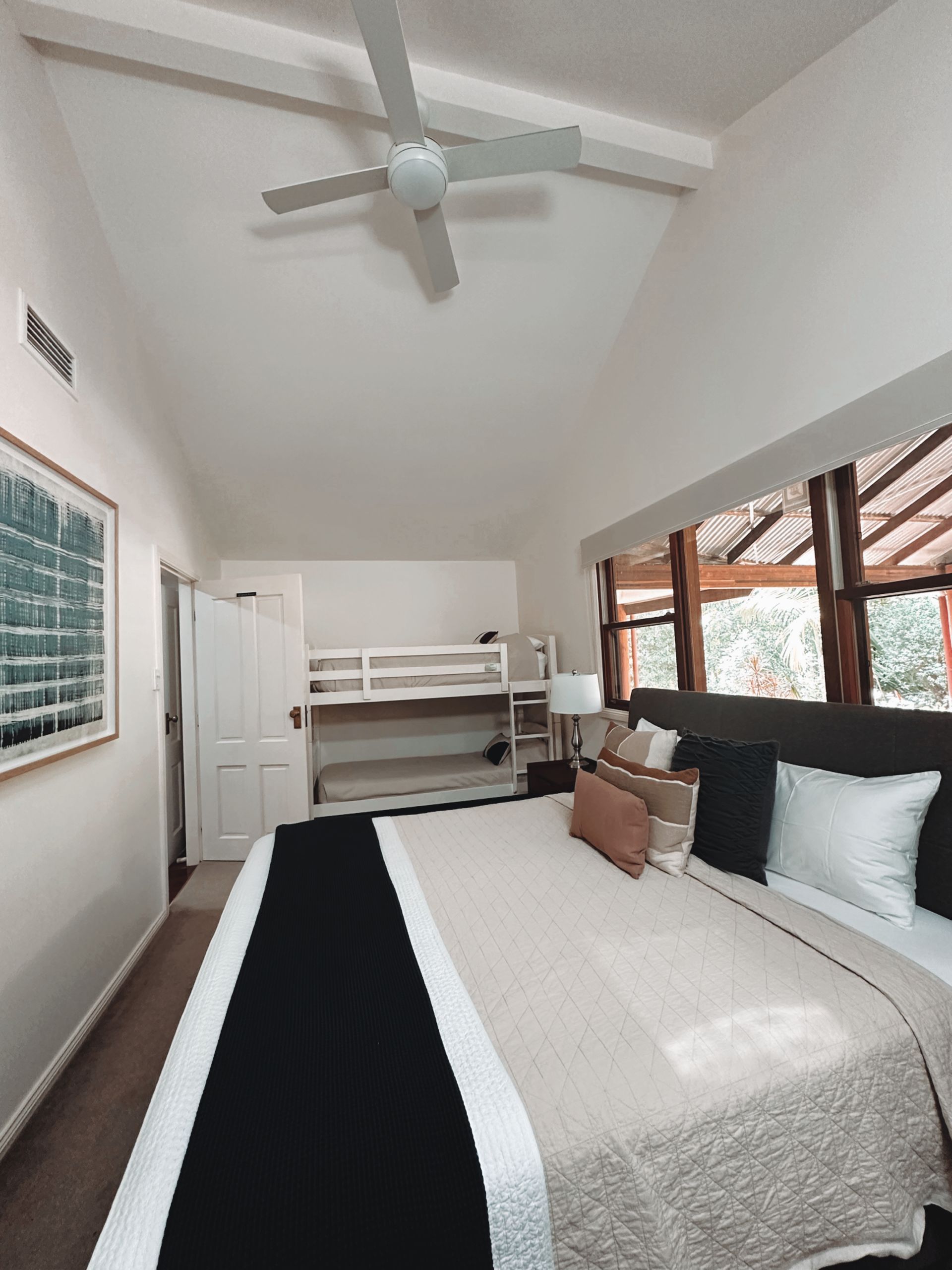 Bedroom with large bed, bunk beds, and ceiling fan. White walls, wood trim, and a window to the outside — Integral Cleaning Services in Aberdare, NSW