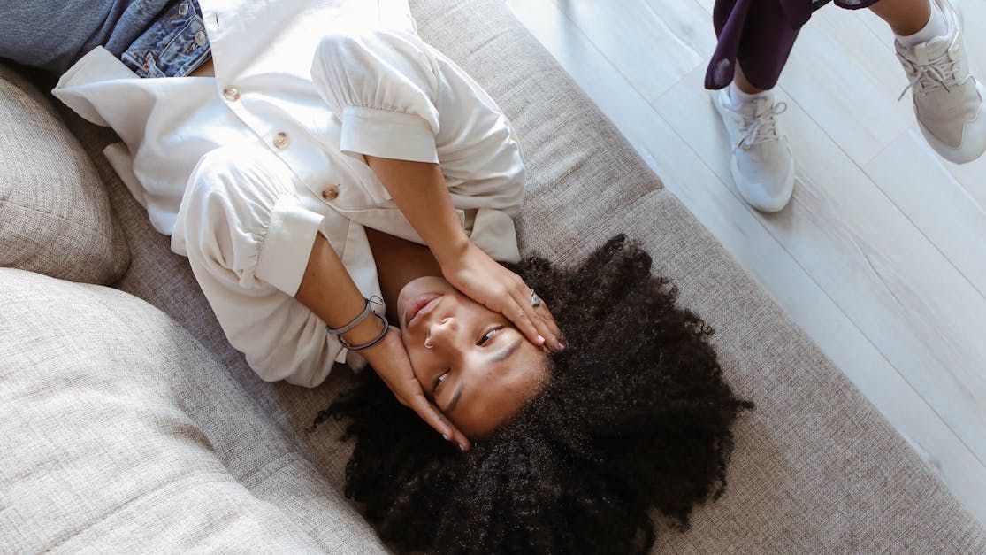 A woman is laying on a couch with her head on her hands.
