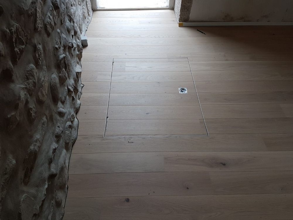 un plancher en bois avec un trou dans le sol à côté d' un mur en pierre