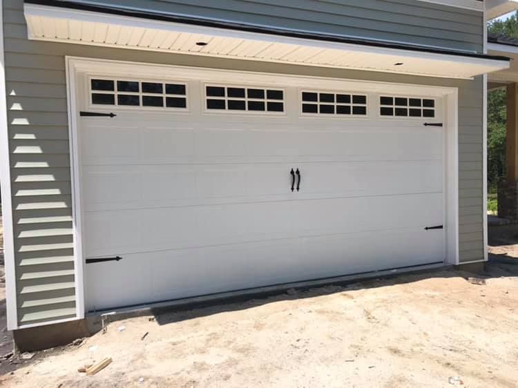 A white garage door with black handles is sitting in front of a house.