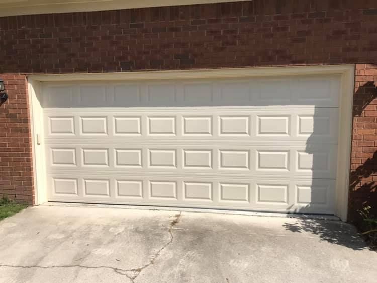 A white garage door is sitting in front of a brick house.