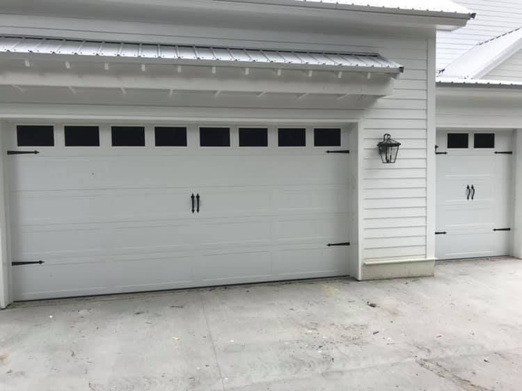 Two white garage doors are sitting next to each other on the side of a white house.