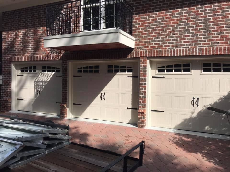A brick building with three white garage doors and a balcony.