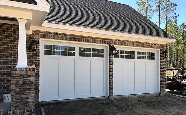 A brick house with two white garage doors and a golf cart parked in front of it.