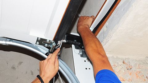 A man is fixing a garage door with a wrench.