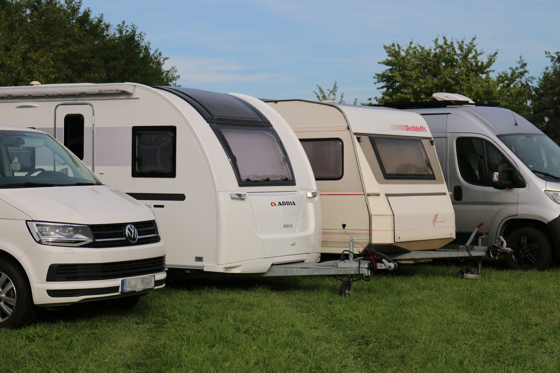 Auf einer Wiese parken mehrere Wohnmobile und Anhänger.