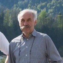 Ein Mann mit Schnurrbart und Brille steht vor einem Wald.