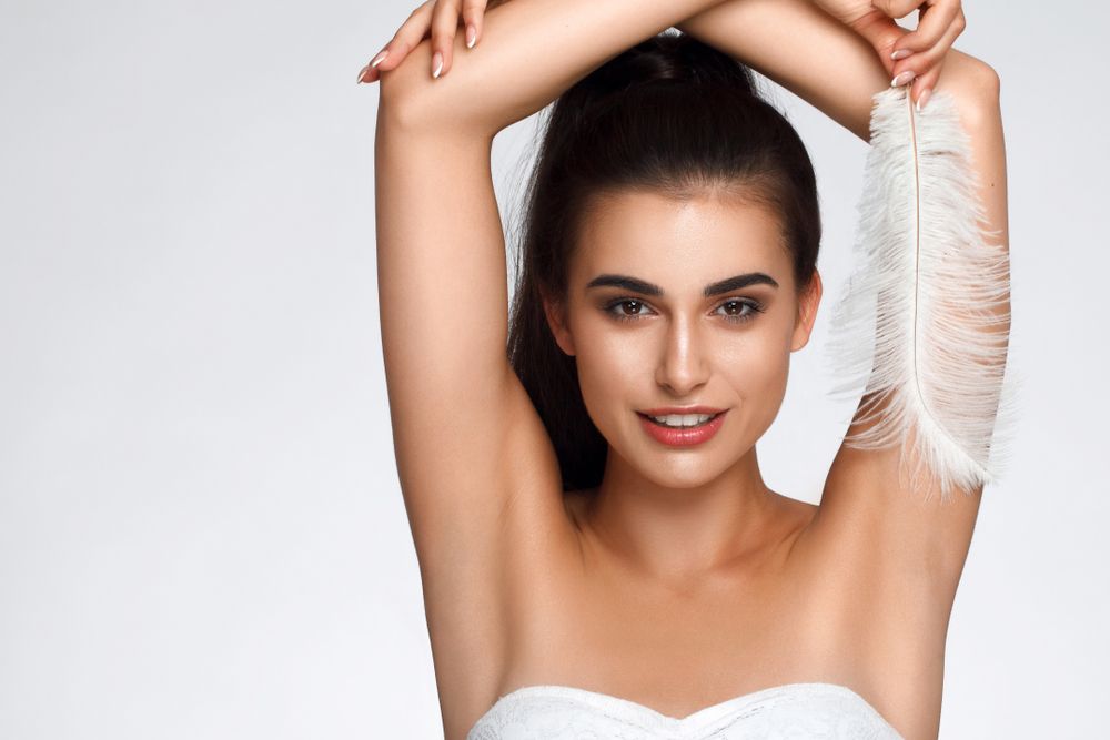 A woman is holding a white feather over her armpit.