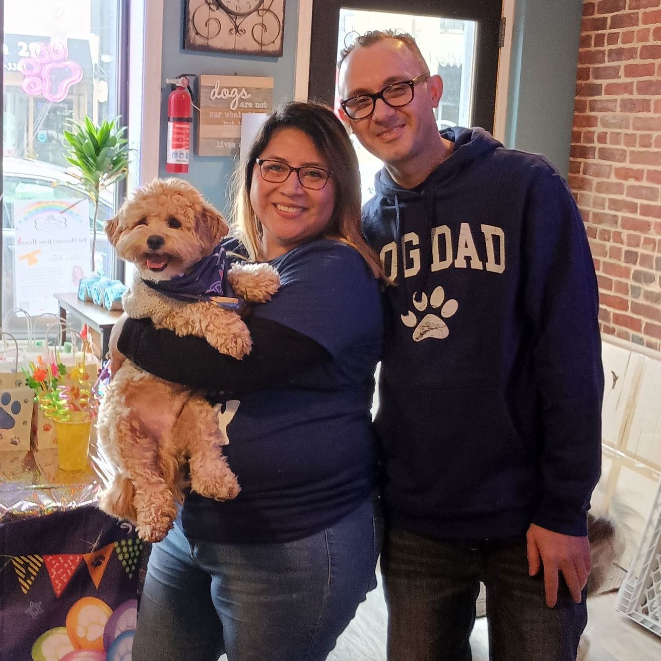 Smiling couple holding fluffy dog inside Smokey’s Doggy Cafe in Keyport, New Jersey