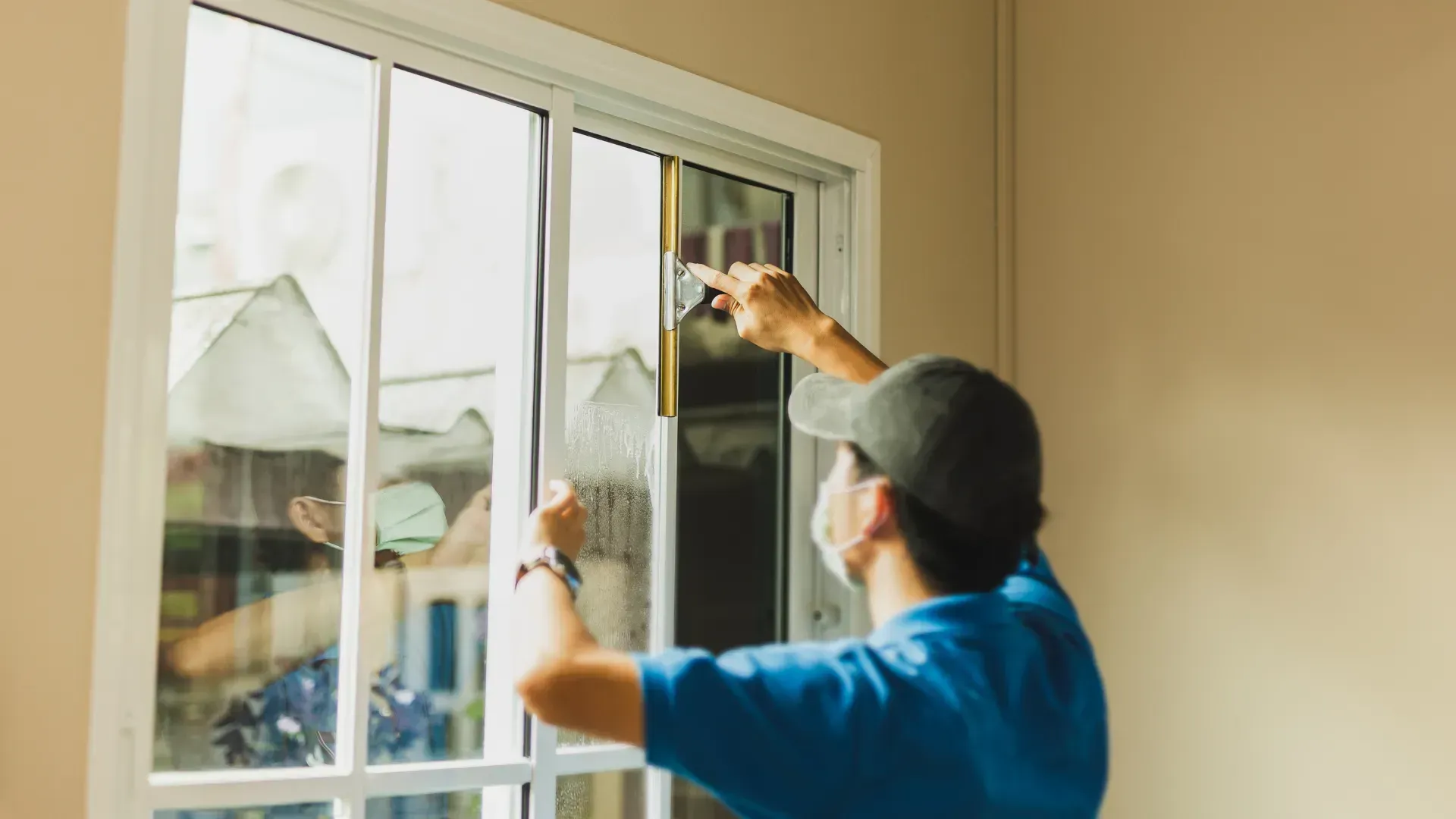 Person applying window film to a sliding glass door, inside a room with beige walls.