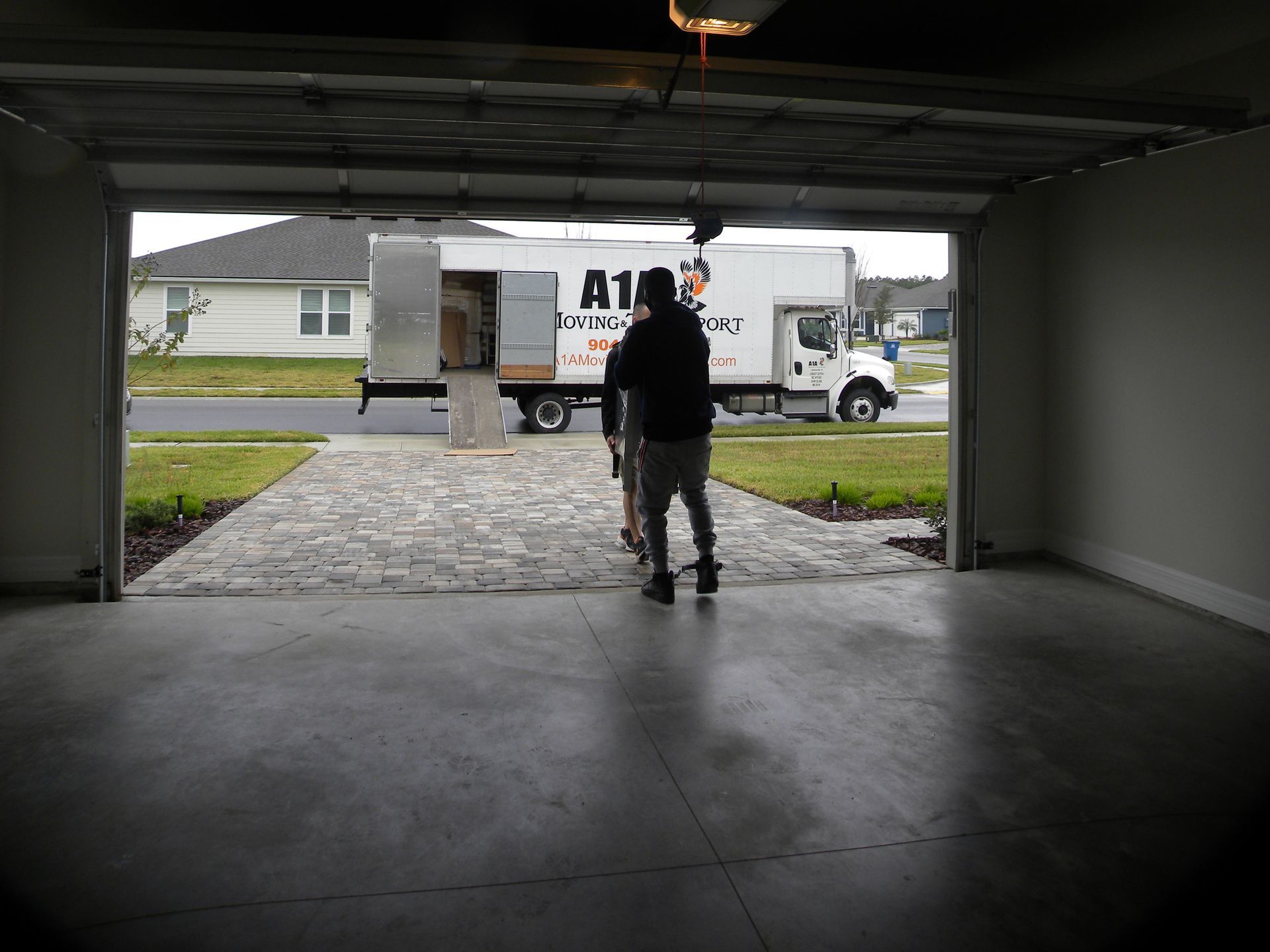Two people in a garage doorway with moving truck in the drive.
