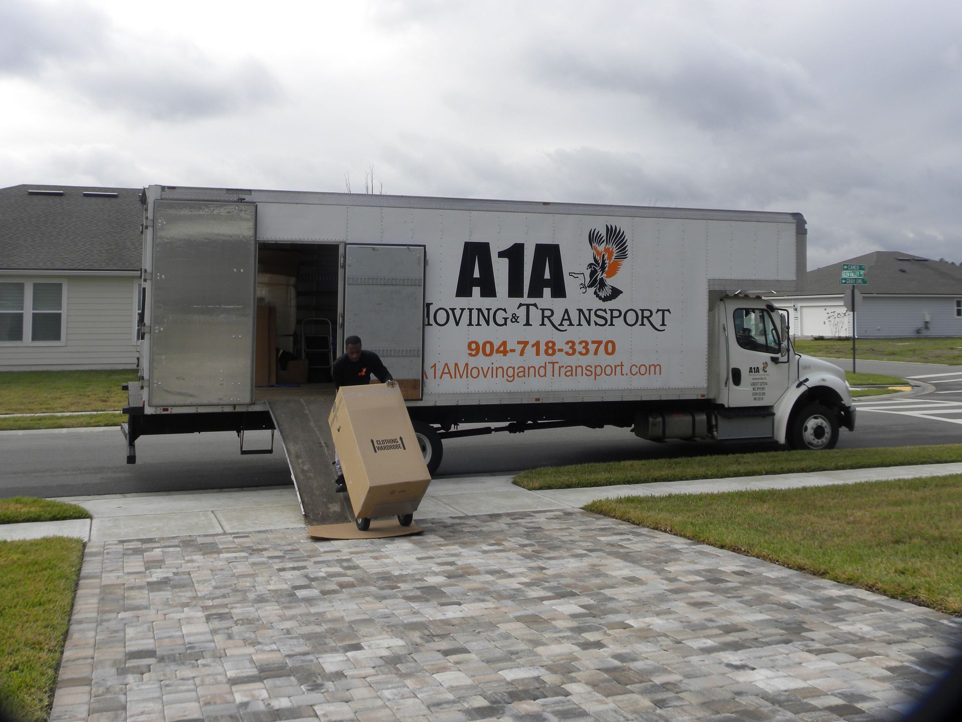 Moving truck parked on a driveway, with a person loading a large box. Cloudy sky.