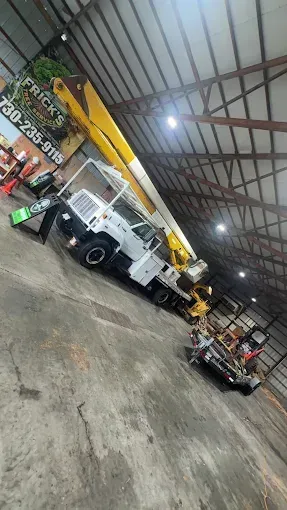 Tilted view of a warehouse with a white utility truck, yellow crane, and parked vehicles inside a large garage