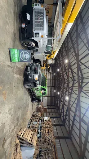 Warehouse with a white utility truck, green forklift, and stacked pallets under a metal roof.
