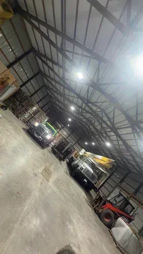 Indoor warehouse with parked cars, a tractor, and bright overhead lights on a metal roof