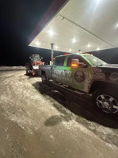 Two tow trucks parked under a gas station canopy at night on a snowy, icy road.