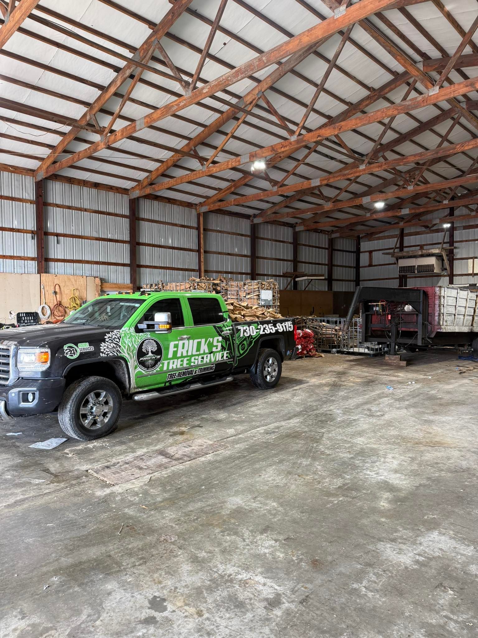 Pickup truck and trailer inside a large metal barn with exposed beams and concrete floor.