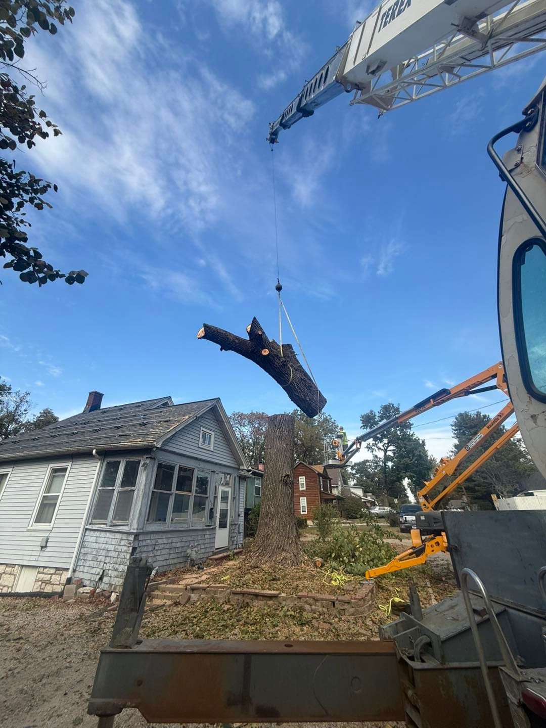 Demolition crane lifting debris beside a weathered white house under a blue sky