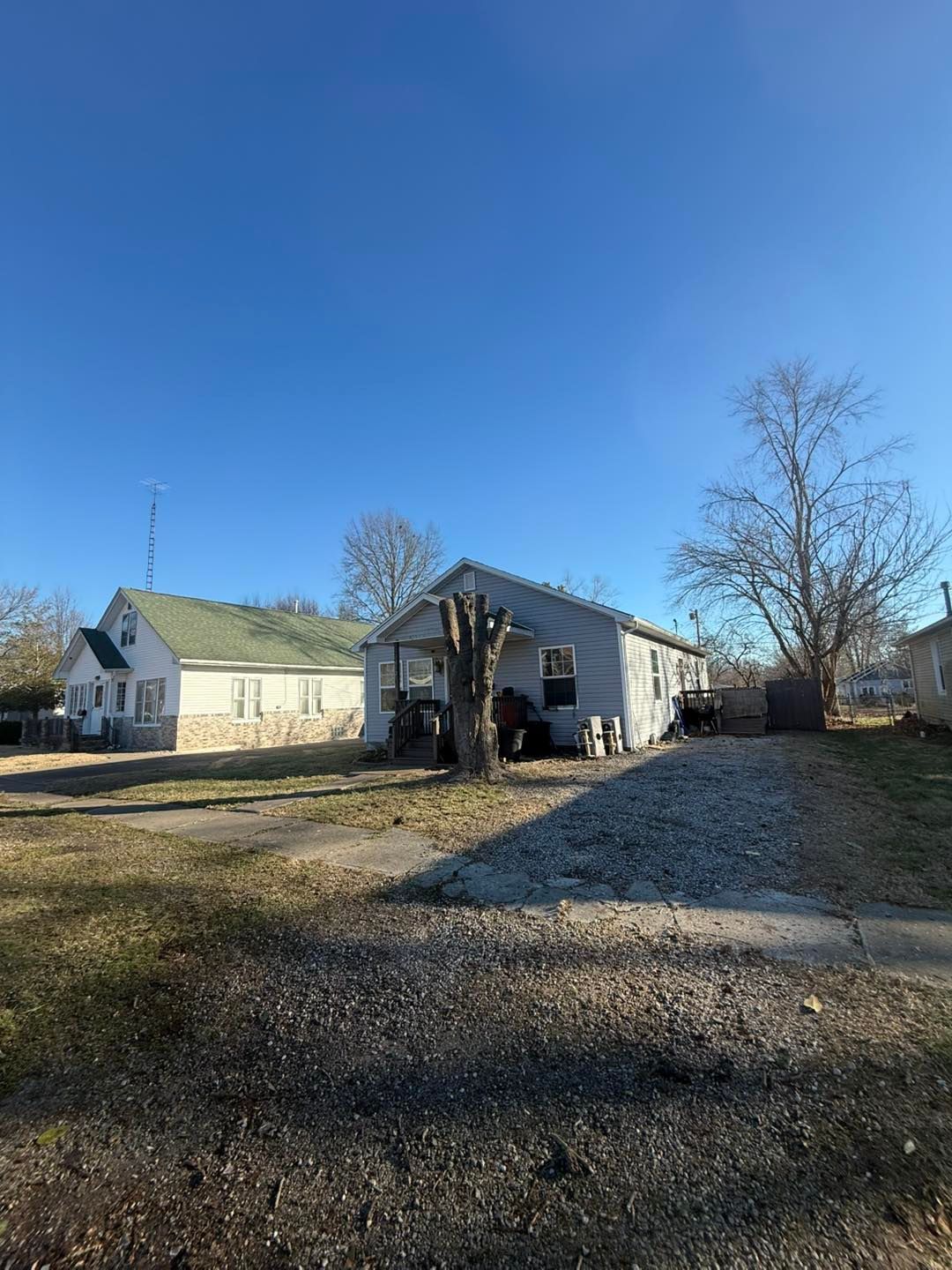 Gravel yard with two small white buildings under a clear blue sky, one partially damaged.