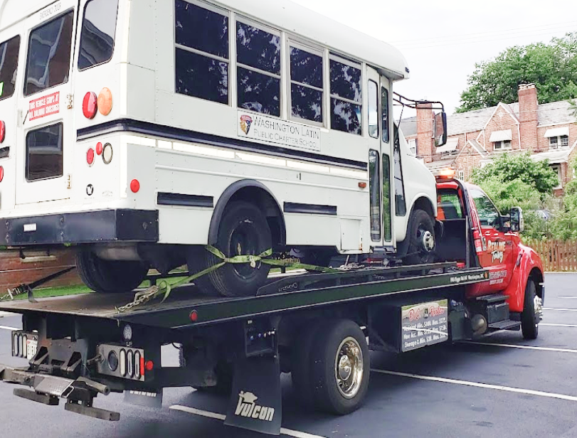 A white school bus is being towed by a tow truck | Action Service Center