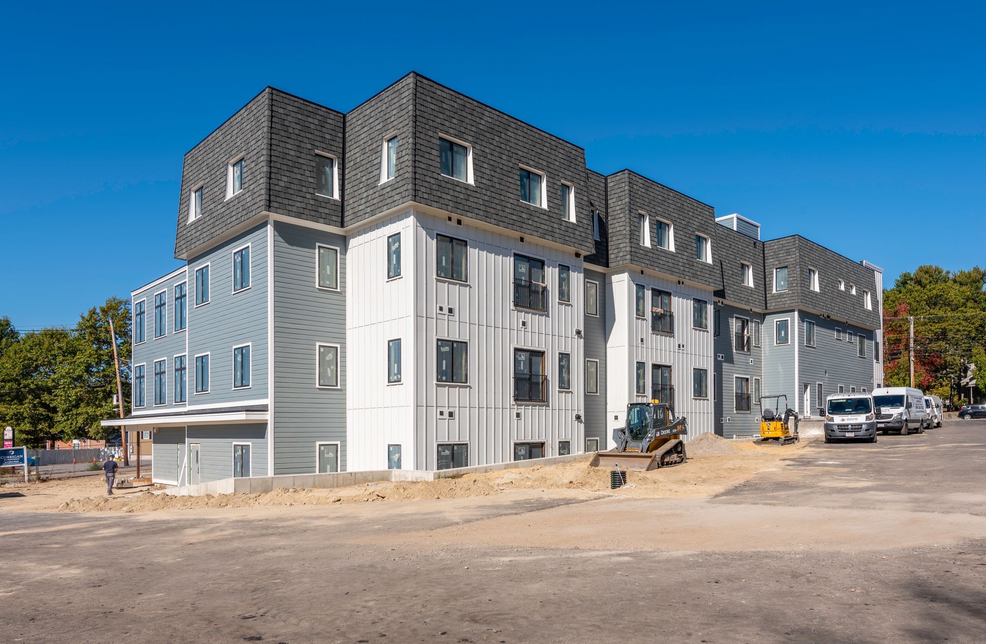 Multi-story building under construction with gray and blue siding, against a clear blue sky.