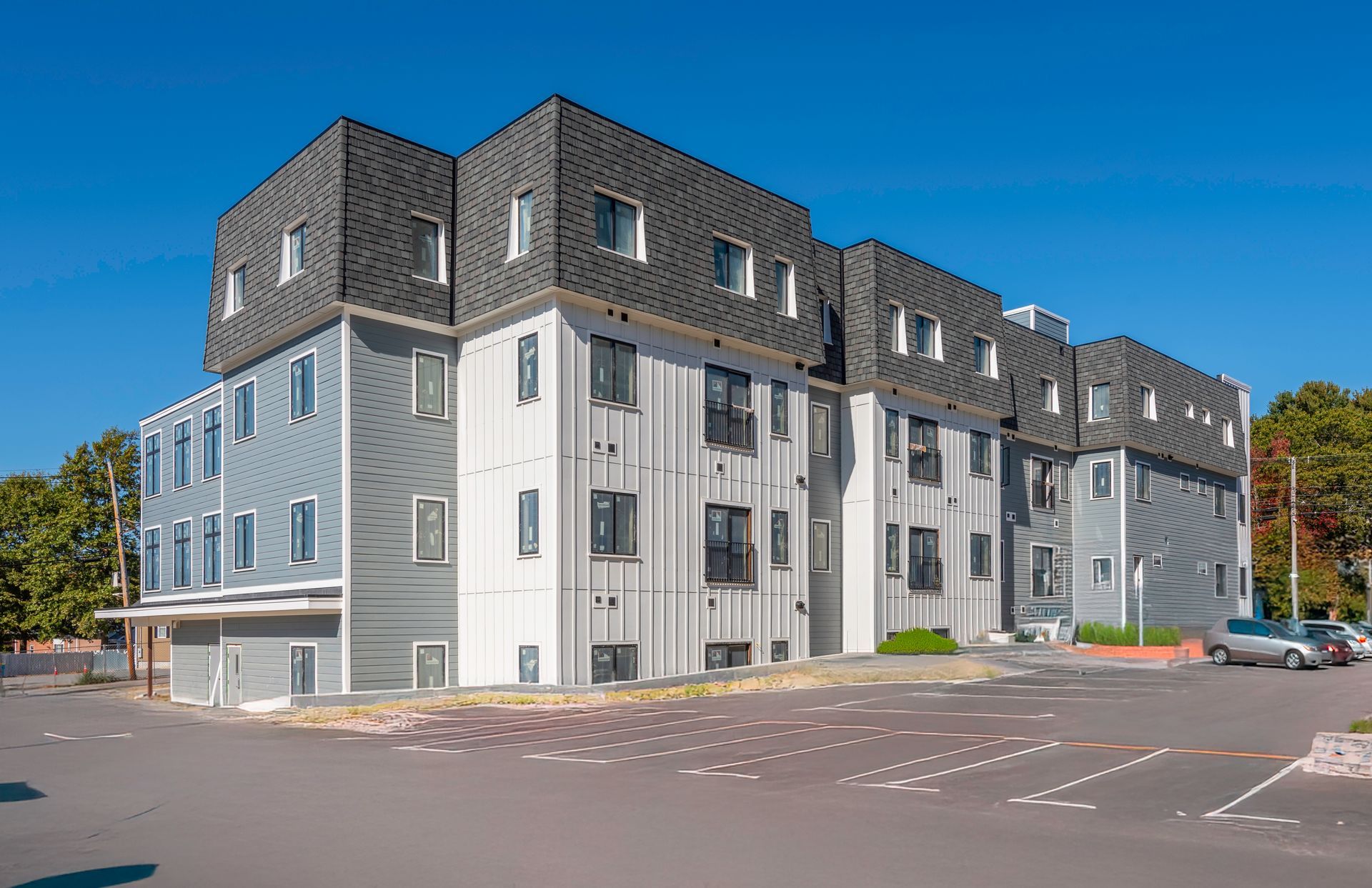 Multi-story apartment building with gray siding and parking lot on a sunny day.