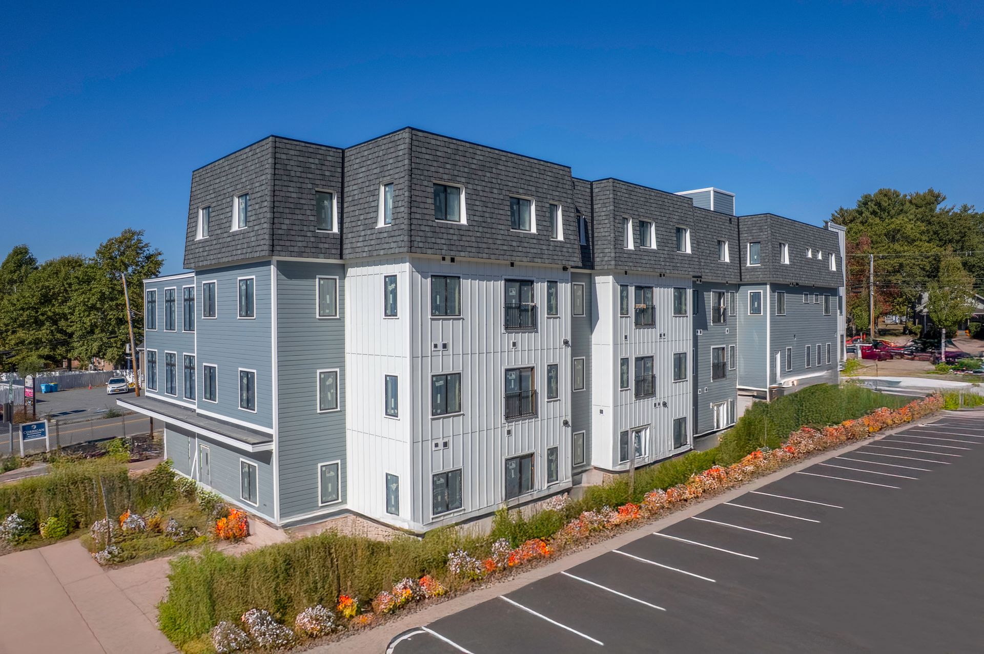 Modern multi-story apartment building with gray and white facade, blue sky, and parking lot.