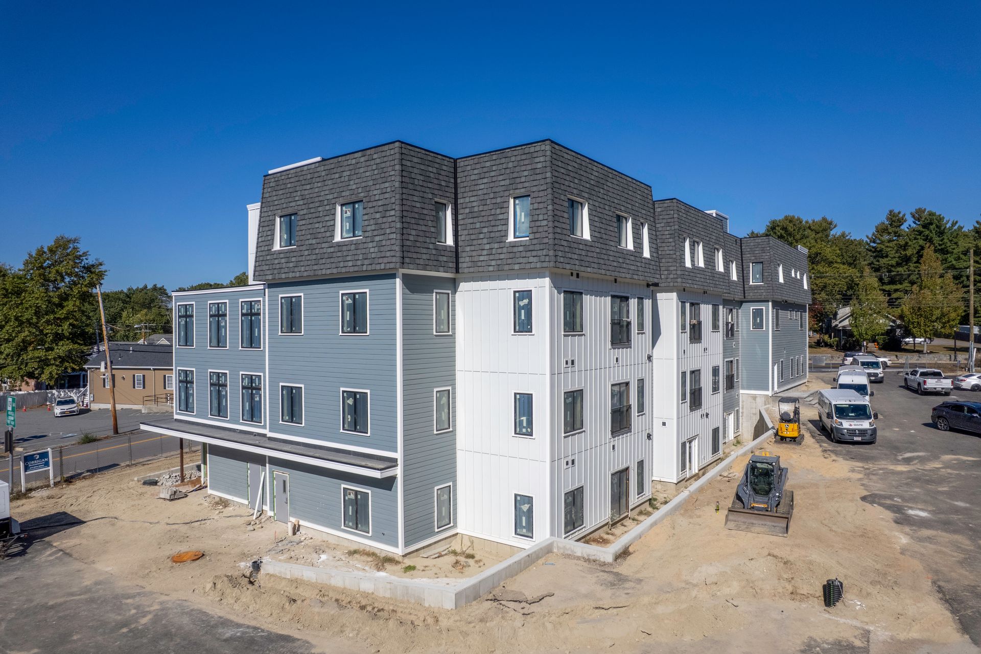 Modern three-story apartment building with blue and gray siding under a blue sky, construction ongoing.