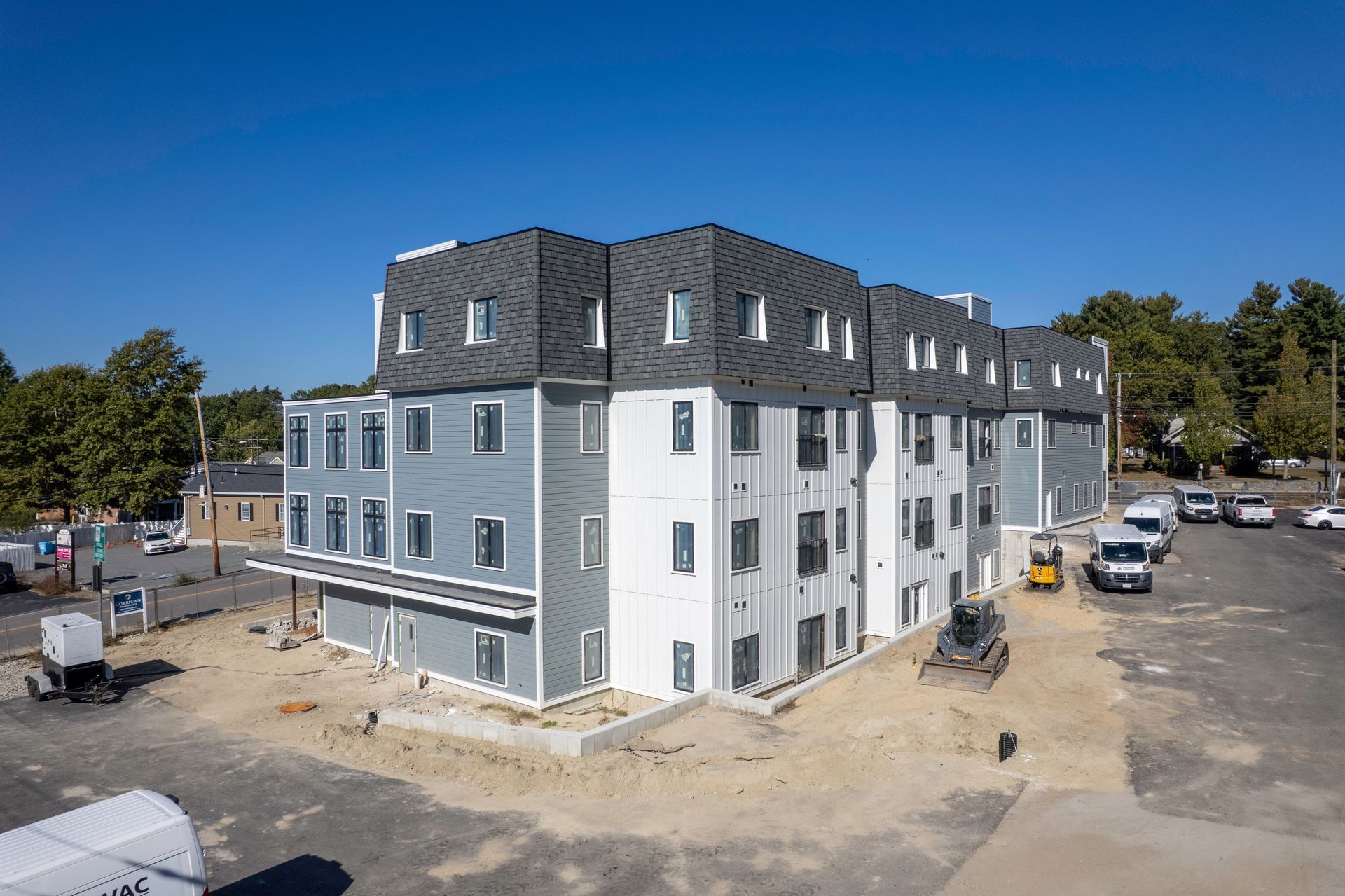 Multi-story apartment building under construction on a sunny day. Gray and white exterior, blue sky.