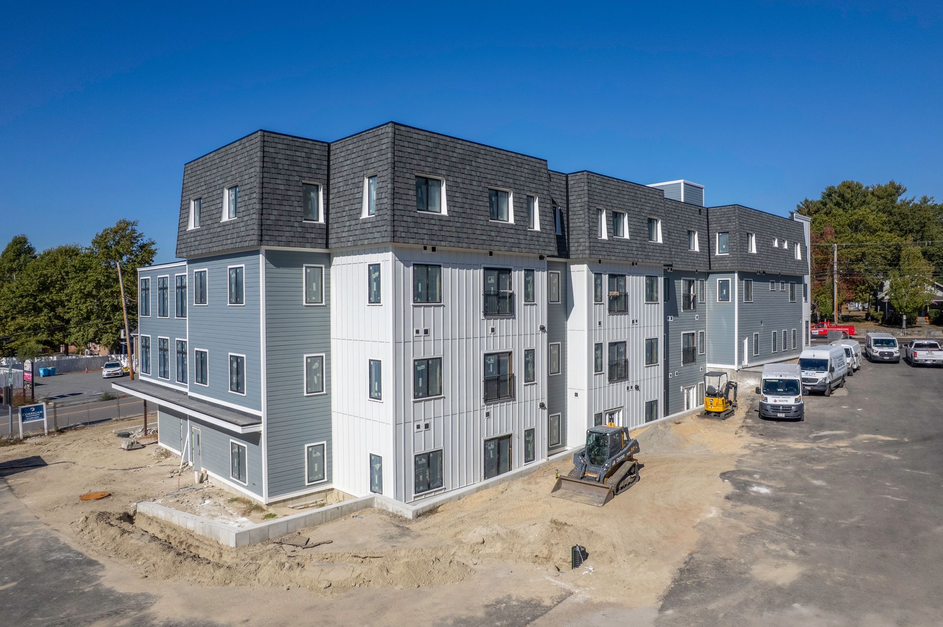 Multi-story building under construction with gray and white siding, blue sky. Construction vehicles present.