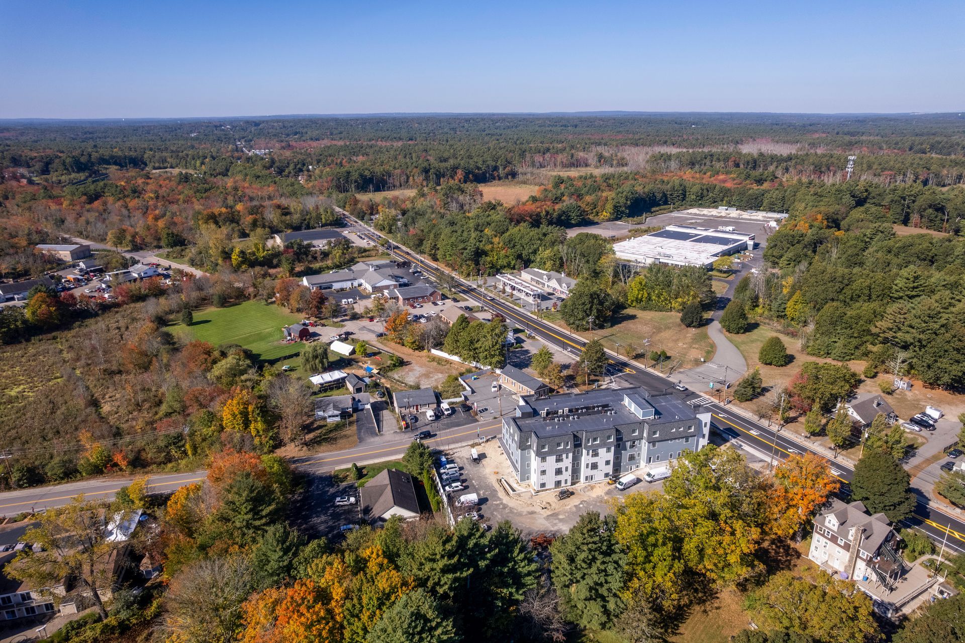 Aerial view of a town with buildings, roads, and trees in autumn colors under a blue sky.