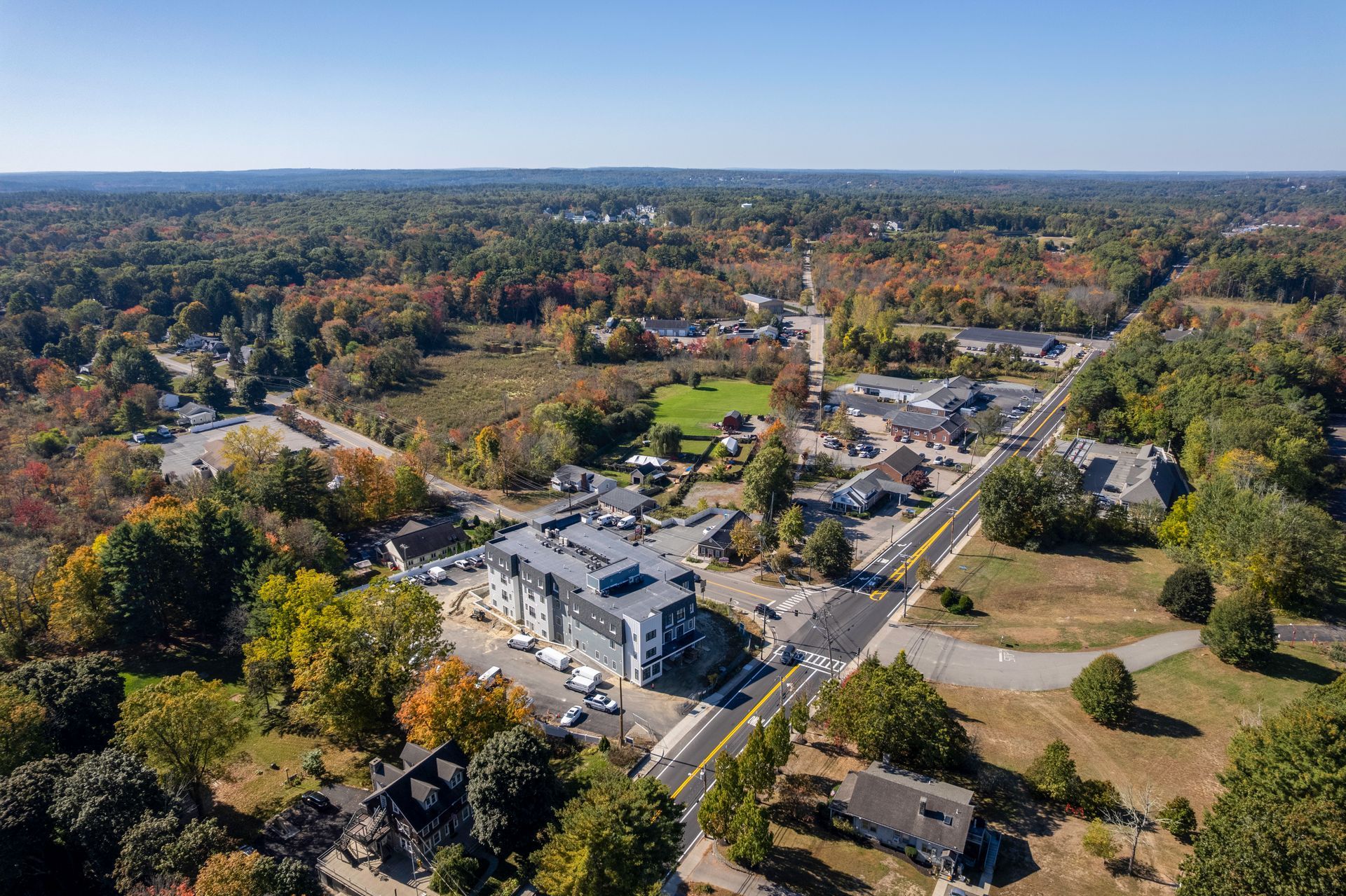 Aerial view of a town with a street running through it, surrounded by trees with autumn foliage.