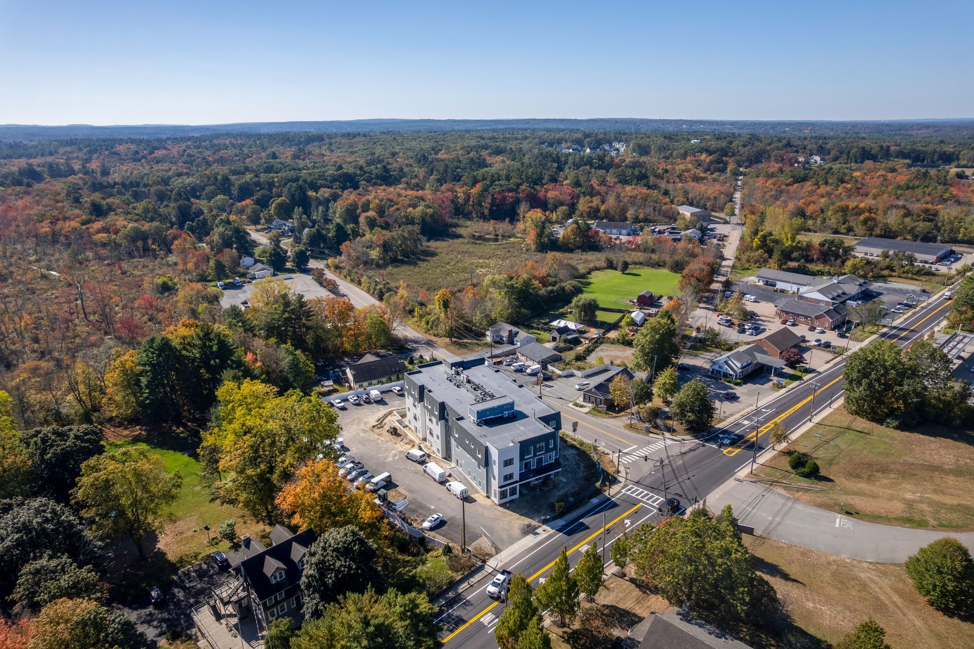 Aerial view of a modern building surrounded by trees and a road, on a sunny day.
