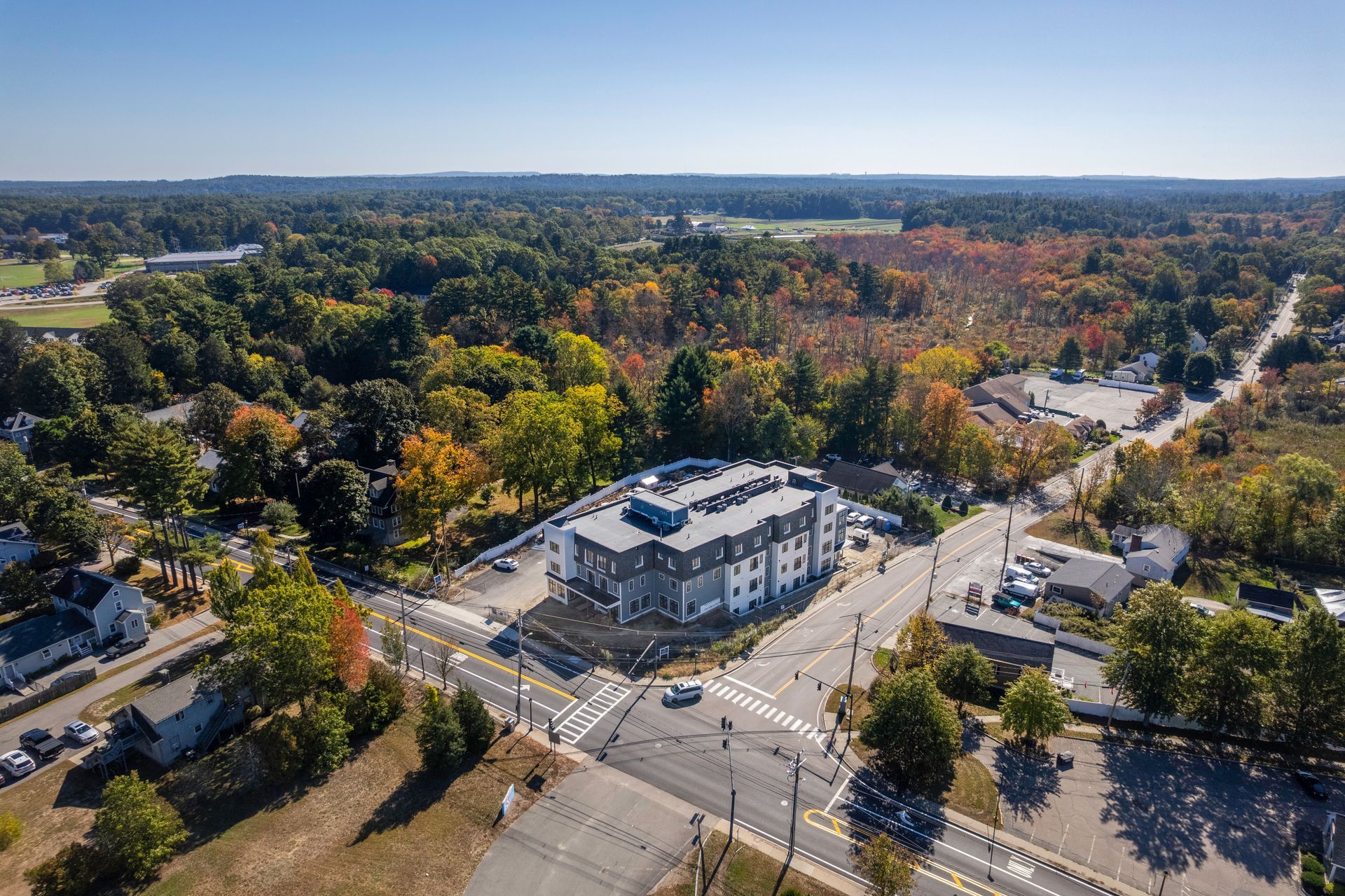 Aerial view of a multi-story building at a road intersection, surrounded by trees and a clear sky.